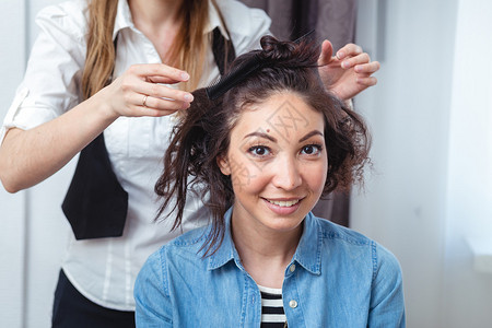 发型师为一个快乐的黑发女人制作卷发美发师在美发沙龙处理黑发女人的头图片