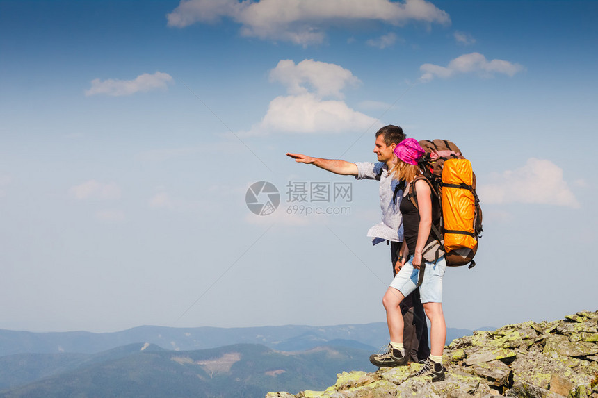 一对背着包的幸福情侣在山上欣赏高处的景色图片