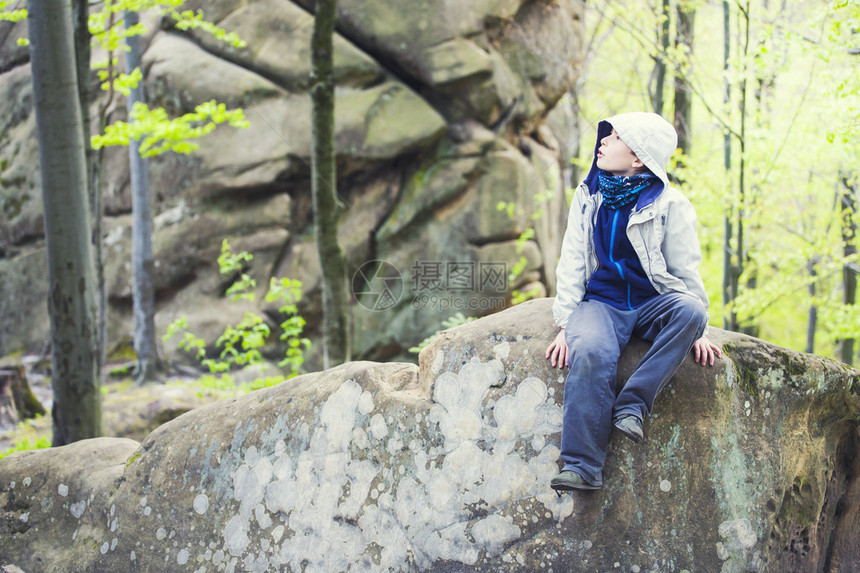 男孩坐在森林的岩石上图片