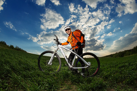 年轻男子骑自行车穿过深草地背着红图片
