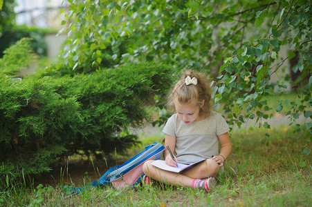 小女生盘腿坐在树下做作业少女的眼神若有所思她的书包躺在女孩旁图片