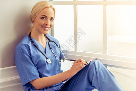 穿着蓝色医服的美丽金发女医生正在做笔记图片