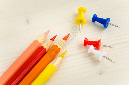 一排彩色铅笔和一张木桌上的图钉图片