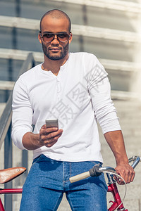 穿便衣和戴太阳眼镜的英俊年轻非裔美国人男子正在使用智能手机图片