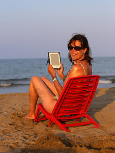 红椅子上的美女在夏天在海边的海滩上读图片