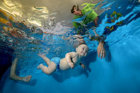 快乐的孩子在蓝色背景的游泳池里训练和游泳图片