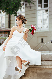 婚纱照拍摄新娘坐在城市的纪念碑附近拿着花束图片