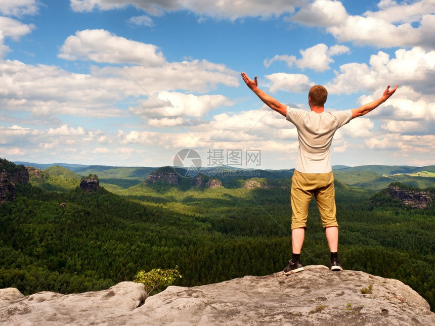 穿着灰色衬衫和在沙石悬崖上漫步短裤的满意徒步旅行者图片