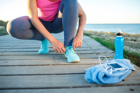 跑鞋系鞋带的女人夏末或秋季女运动健身跑步者准备在海滨户图片