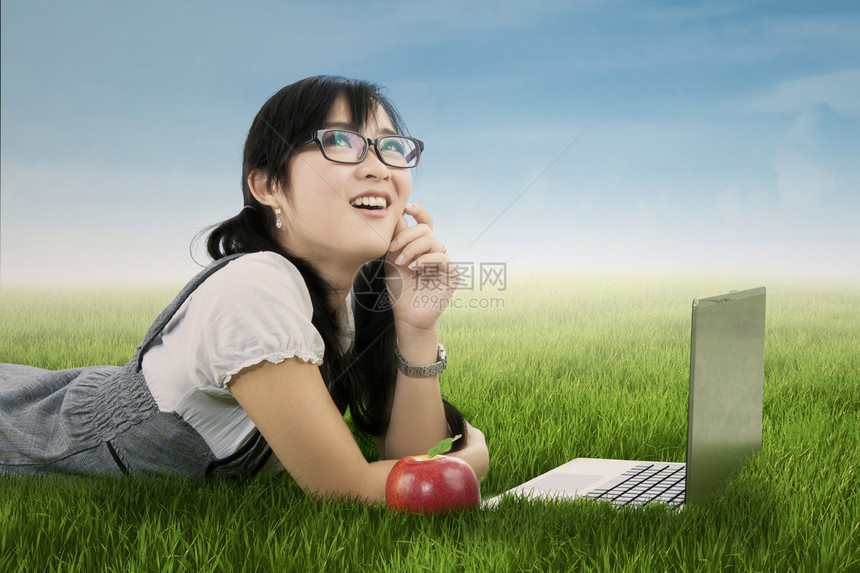 高中女生在草地上用笔记本电脑和红苹果做图片