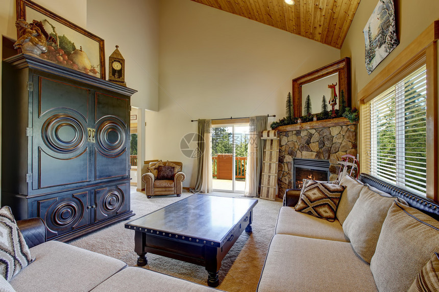有高木拱形天花板和地毯板的舒适客厅配有大米色沙发橱柜和带抽屉的黑色咖啡桌角落里还有天然石图片