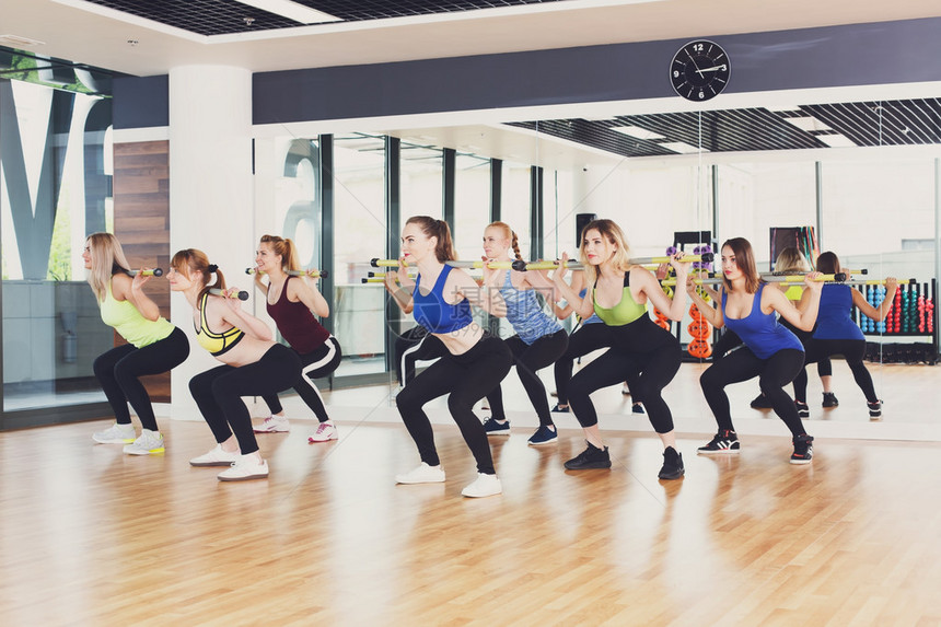 一群在健身课上锻炼的年轻女女孩用杠铃做深蹲健身俱乐部的健康生活方图片