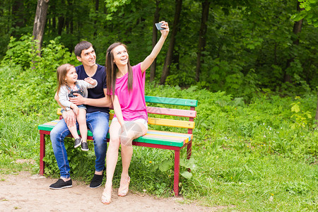 快乐的年轻家庭用智能手机在公园拍自图片