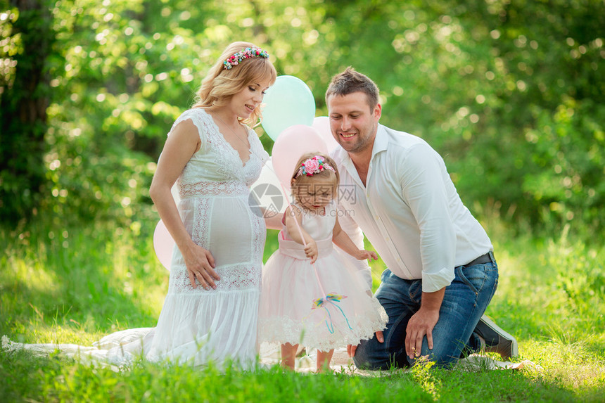 美丽的孕妇与她的丈夫和年轻的女儿一起在绿花园图片