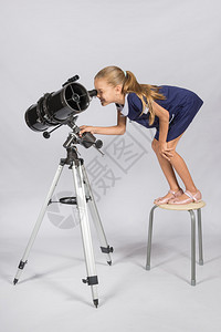 年轻的天文学家站在椅子上滑稽地看着望远镜图片