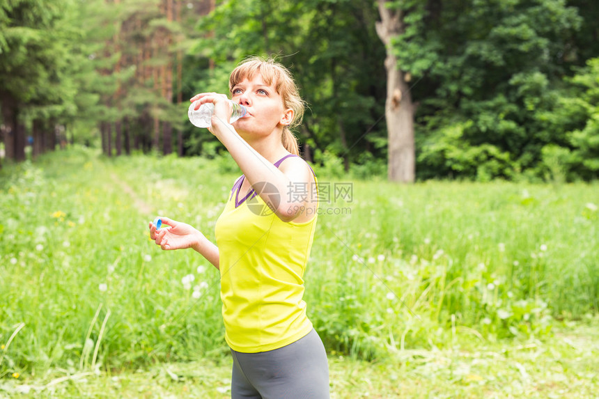 年轻女子慢跑后从塑料瓶里喝水女孩在户外健身后解渴健图片