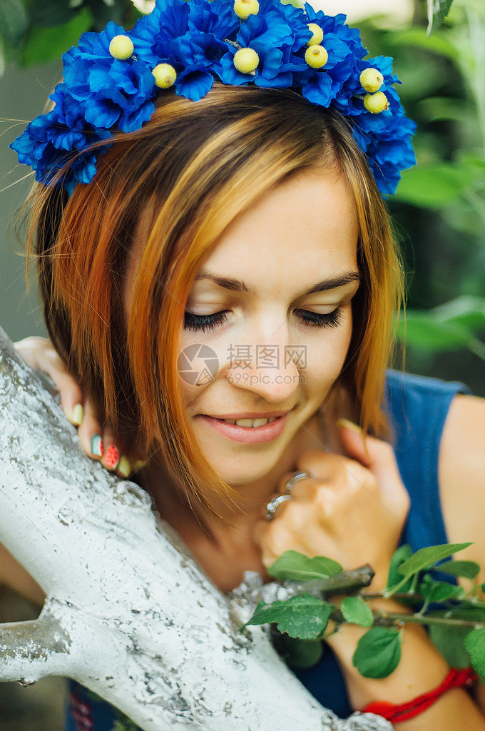 一个戴着花圈的美丽年轻女子的画像年轻漂亮的女人和她头上的花束合影夏天在户外用人造花装饰花环图片