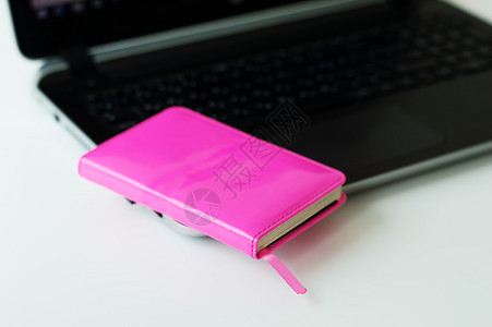 黑计算机粉红纸笔记本小商业日记和白办公室桌上图片