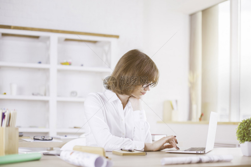 商业妇女用膝上型笔记本电脑在乱七八糟的台式计算机上使用图片