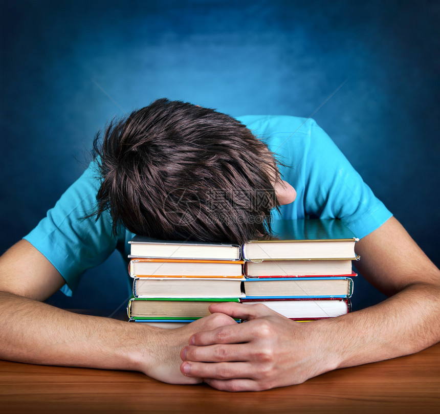 疲倦的少年睡在蓝色背景的书上图片