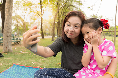 母亲用智能手机教女儿亚洲母女在花园图片