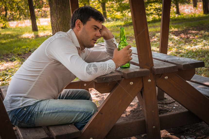 单身醉酒男子坐在长椅上在公园图片
