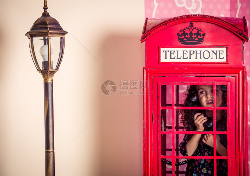 一个小女孩在传统的红色电话亭图片