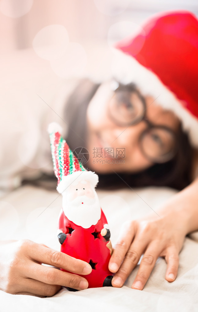 手持圣诞老人玩具躺在白床上双与bokeh光线有图片