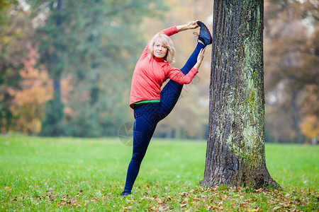 年轻微笑快乐的女人在秋季公园做瑜伽图片
