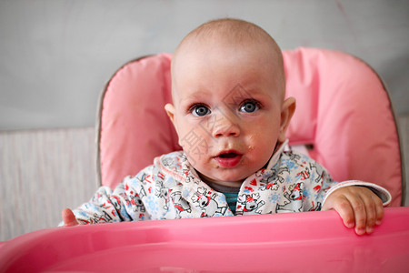 美丽的婴儿吃妈手的粥他坐在粉色儿童椅图片