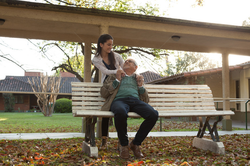 年轻女人和她的祖父坐在长凳上在秋天公园里图片