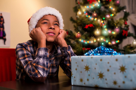 悲伤的美国黑人男孩在圣诞节坐在圣诞礼物旁边的孩子最好去看烟花在圣图片