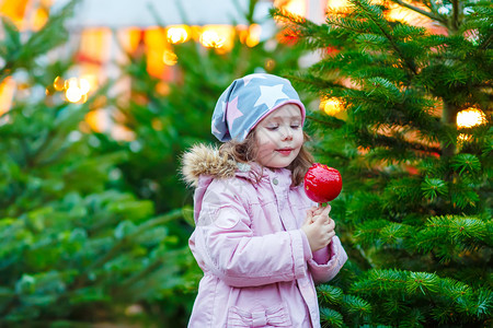 可爱的小女孩在圣诞节市场上吃糖苹果图片