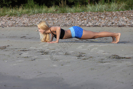 在沙滩上做俯卧撑的健身年轻女子图片