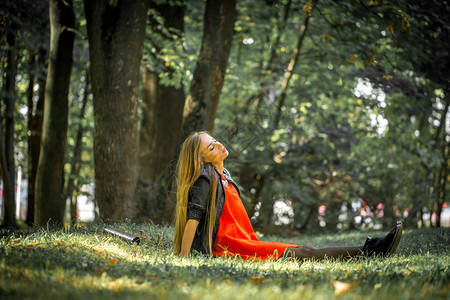 穿着红裙子长发的漂亮女孩和穿皮夹克的女孩坐在草地上图片
