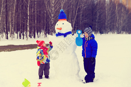 男孩和女孩与大自然中的雪人玩耍孩图片