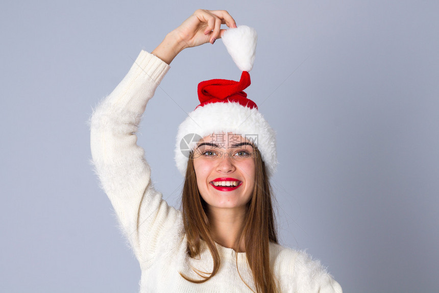 穿着白毛衣的年轻迷人女戴着红圣诞帽在工作室里拿着灰图片