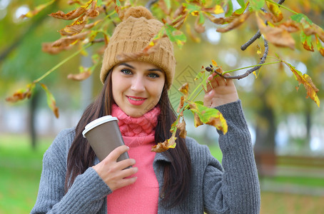秋天在公园里戴着甜瓜帽的美丽的年轻女子拿着咖啡杯图片