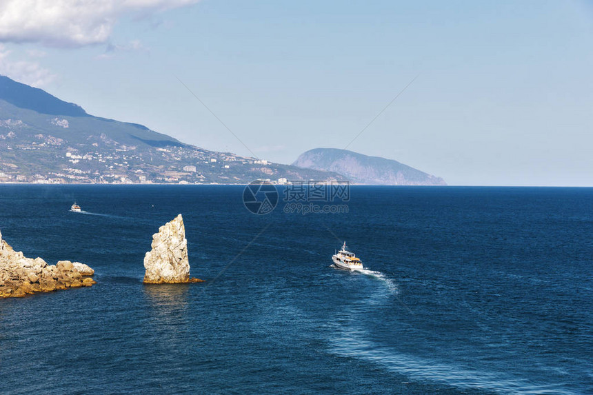 在蓝海背景下沿着岩石海岸航行的游艇蓝色图片