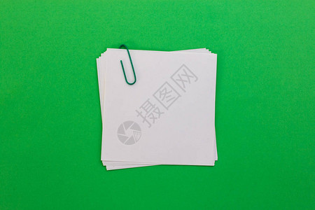 绿色背景上带有绿色回形针的白纸图片