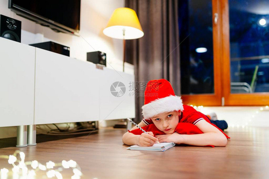 沉思的小男孩给圣诞老人写了一封信戴着红色圣诞老人帽图片