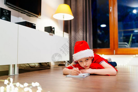 沉思的小男孩给圣诞老人写了一封信戴着红色圣诞老人帽背景图片