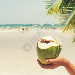 由妇女掌管的新鲜椰子鸡尾酒在热带海滩上图片