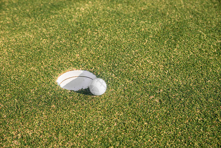 高尔夫球坐在放绿色的洞口的嘴边高尔夫图片
