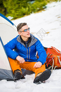 男子在冬天穿过山上时坐在帐篷附近图片