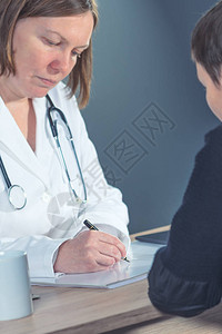 医生在体检后为医院办公室的女病人撰写医学治疗处方图片