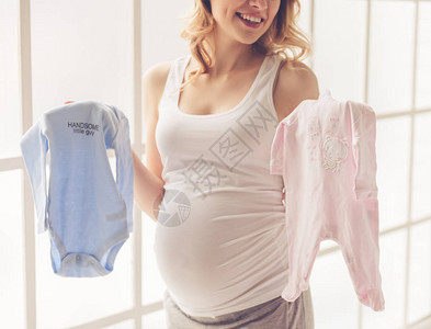 美丽的孕妇穿着婴儿体服和微笑着图片