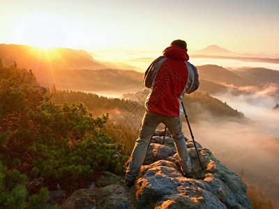 快乐的摄影爱好者喜欢在岩石上的悬崖上拍摄大自然中的秋天黎明图片