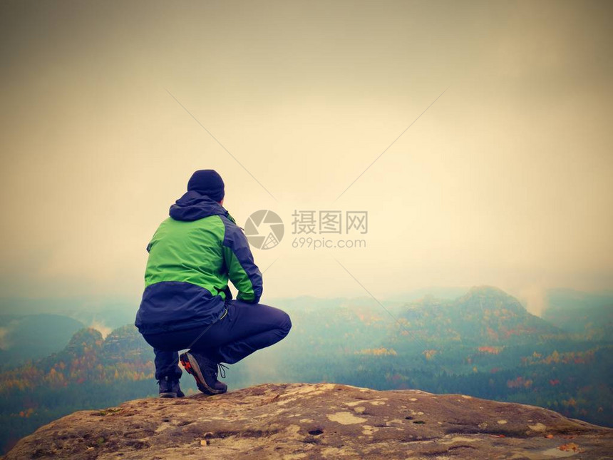 身穿黑色运动服的年轻人坐在悬崖边上看着迷雾的图片