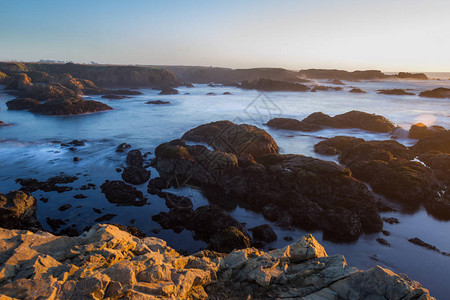 和平放松的场景与海浪撞向加利福尼亚州海滩的岩石海岸线在日落时以慢速图片